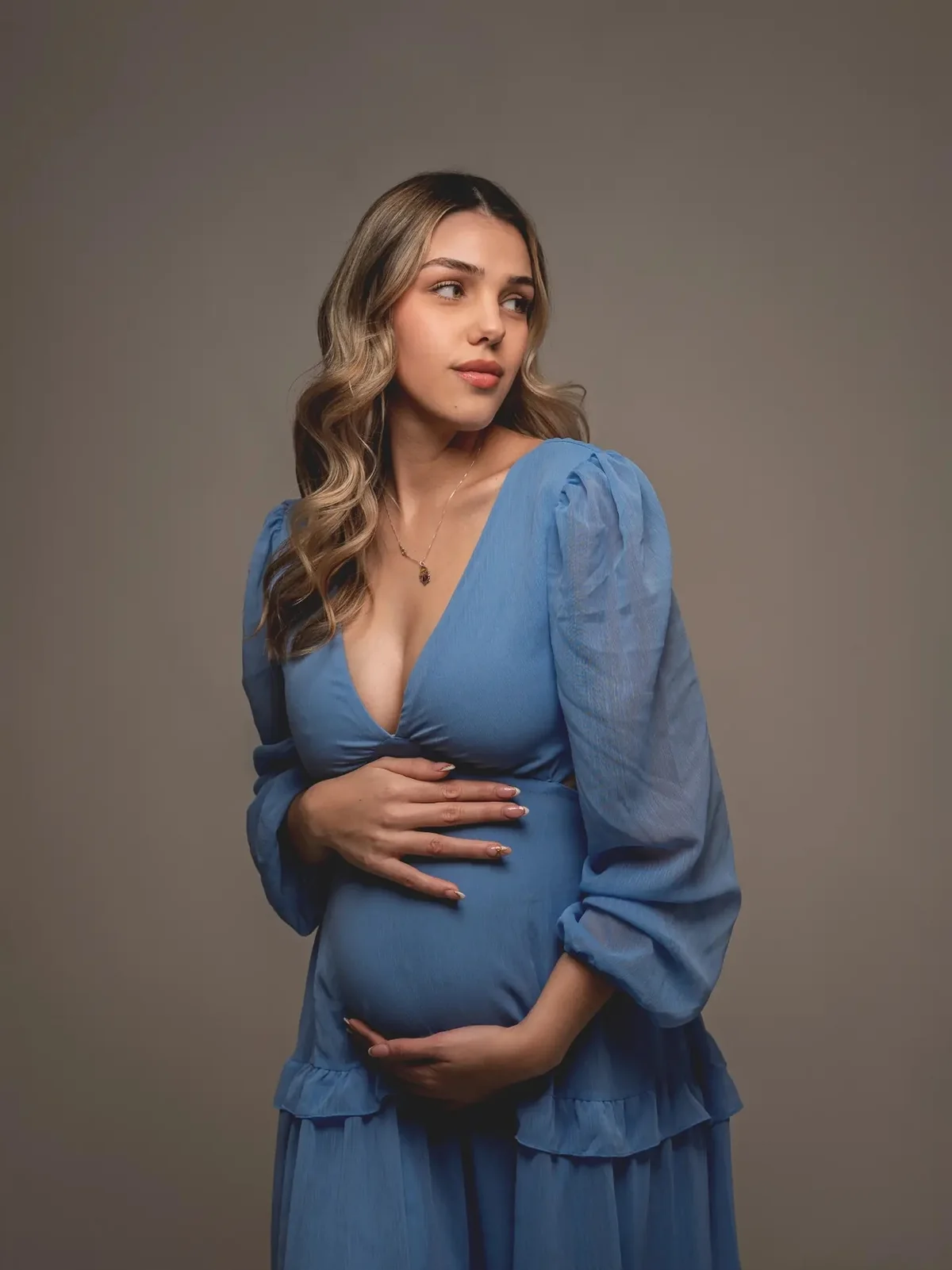 Embarazada con vestido celeste tomándose la panza en el estudio