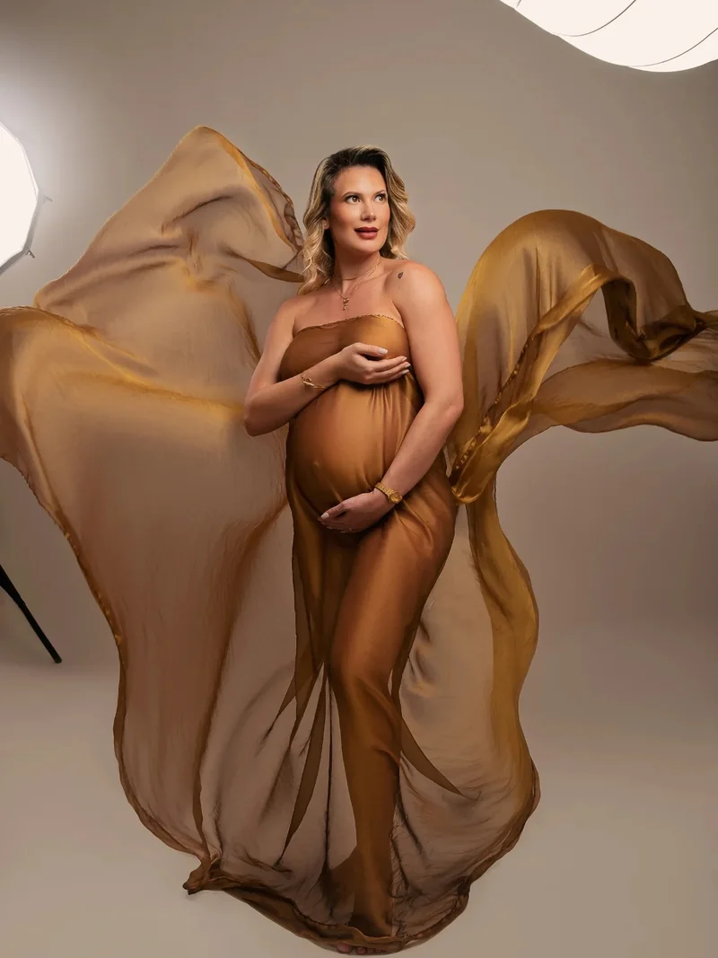 Embarazada con tela dorada al viento, foto editorial